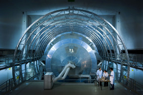 The KATRIN experiment with scientists in front of it. It has a massive set of metal rings around a metal disk 