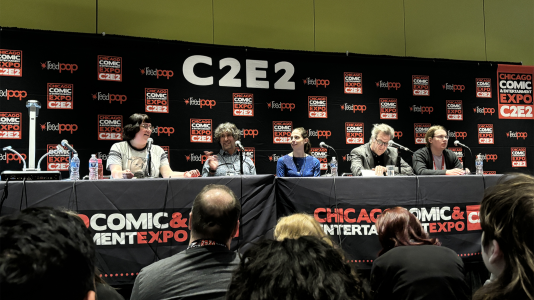 A panel of scientists and science communicators at a table on a stage at C2E2 with people in the audience