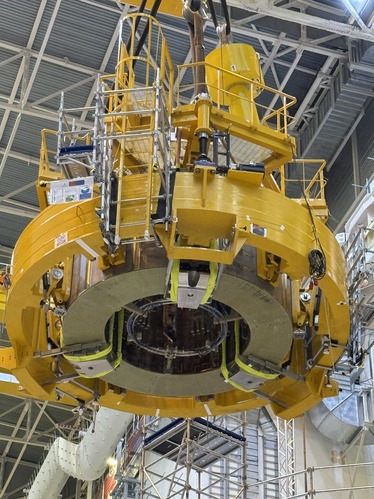 Photo of the solenoid module, a large yellow double-ring with additional equipment on top, getting lowered down