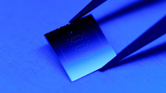 A quantum computer chip being held by tweezers against a blue background