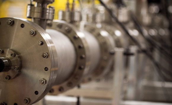 A large metal pipe with ring fittings around it that is part of an accelerator beam 