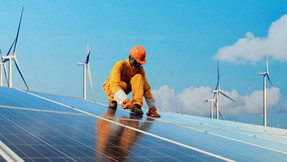 Worker installing solar panels with windmills in the background