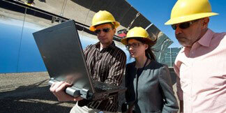 Workers with hardhats looking at a laptop on job site.