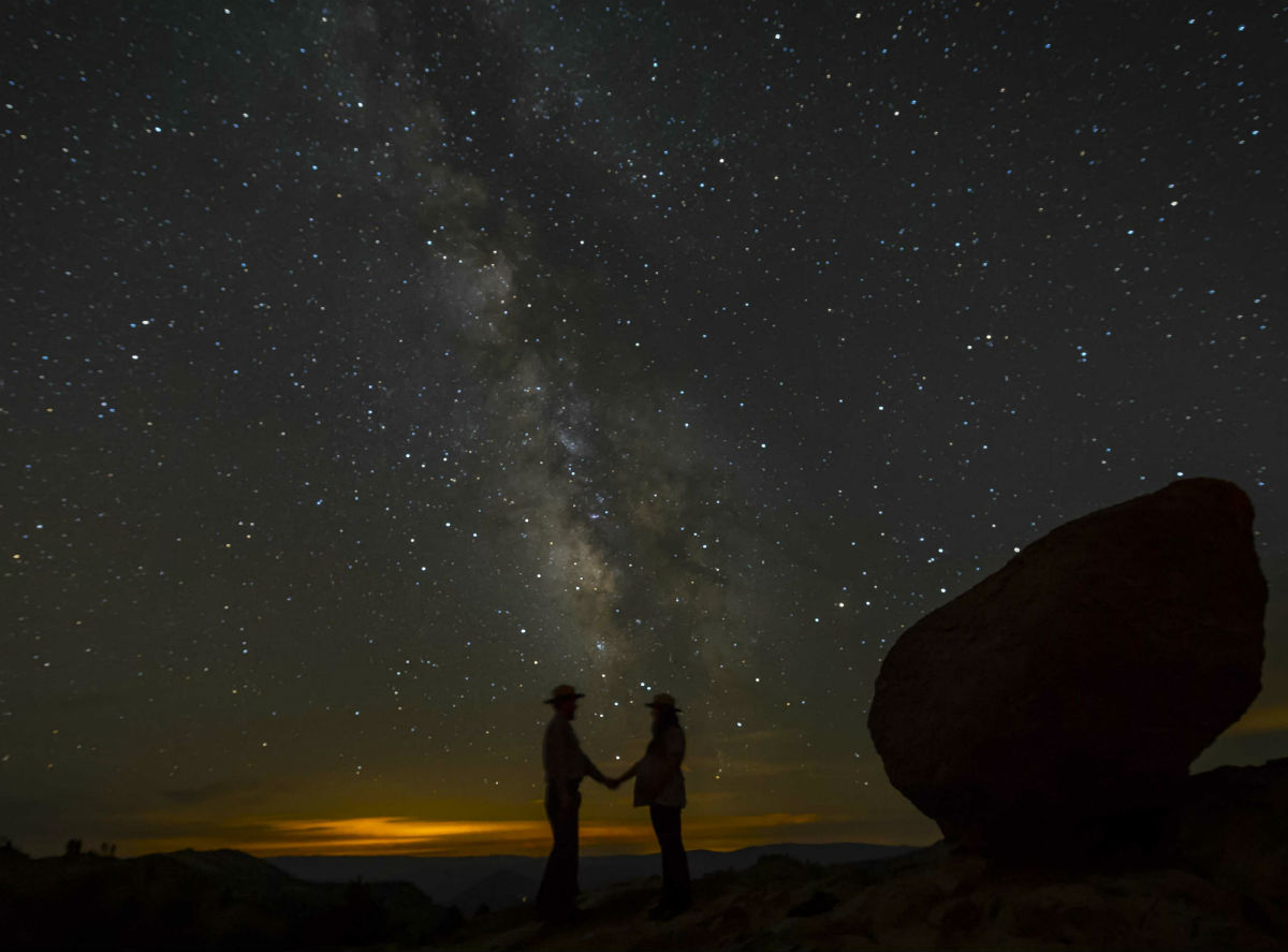 Two people in wide hats stand under a starry sky holding hands.