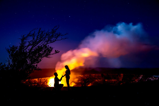 Two people share a romantic moment next to a flaming, smoking crater at Hawaii Volcanoes National Park.