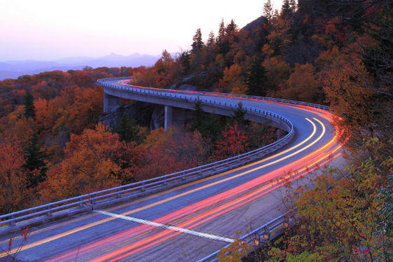 The blue ridge parkway curves along a mountainside past trees wearing autumn leaves.