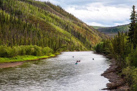 Kayakers float down the expansive Fortymile River that is flanked by hills.
