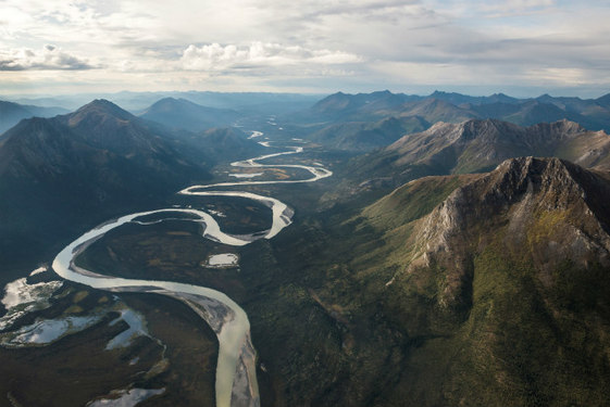 A river curves dramatically through a wide valley between two lines of mountains.