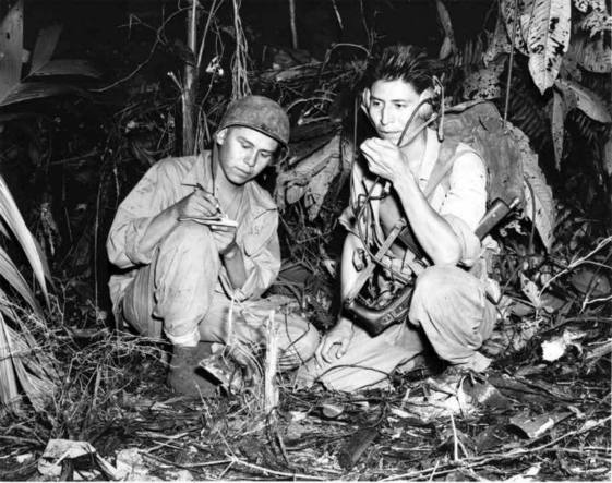 Historic black and white photo of two Native American Code Talkers operating a radio in the jungle. Photo by U.S. Marine Corps.