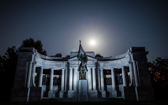 A bronze statue of a soldier carrying a flag and riding a horse stands in front of a wide white marble memorial.