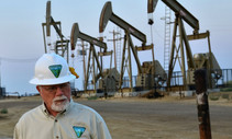 A photo of a BLM employee in a hard hat with oil rigs in the background.