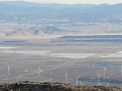 A desert valley with solar panels and wind turbines.