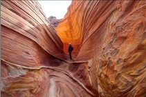 A hiker in a ravine of red slick rock.