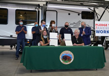 People standing and sitting behind a table after signing a pledge.
