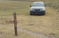 Car parked in a field behind a No Vehicles sign.