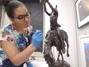 Intern wearing gloves cleaning a bronze sculpture of an American Indian on a horse.