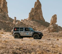 Two off-road vehicles parked in front of rock formations in the desert.