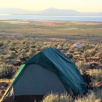 Camping tents in a brush covered field overlooking a lake and agricultural area.