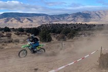 A motorcycle rider driving on a dirt trail with mountains in the background.