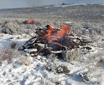 A pile of wood burning on a snow filled landscape.