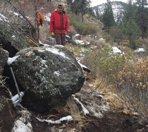 A large boulder blocks a dirt trail as a man stands behind it.