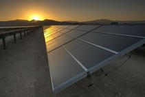 Solar panels on a dry landscape with a sunset in the background.