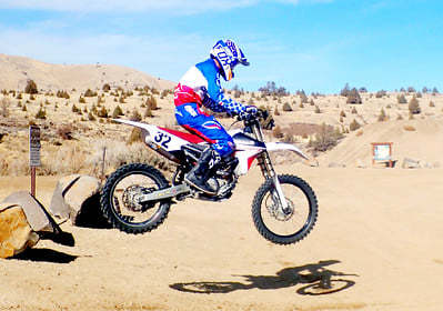 A person on a dirtbike jumping in the air in the desert.