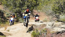 Dirtbike racers jumping large rocks on a trail.