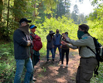 People standing on a forest trail listening to a trail guide.