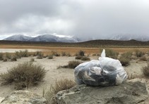 A bag of trash sitting on a rock in a desert.