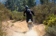 A dirtbiker riding on a dirt trail through a forest.