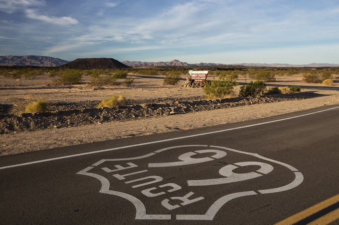 A roadway that reads Route 66 with a large crater mountain in the background.