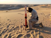 A man putting an orange pole in the sand.