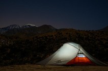A tent illuminated at night in front of a mountain range.