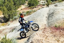 A motorcycle rider riding up a large rock surrounded by trees.