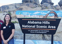 A woman standing next to a sign for the Alabama Hills.
