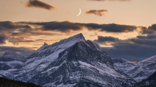 A sliver of moon hangs just above the mountains