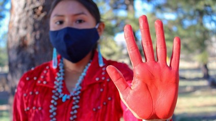 a person in a red dress holds their red painted hand up towards the camera