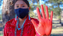 A native American holding her red painted palm in front the camera.