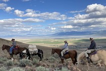 4 horse pack string: 3 riders and gear with backdrop of valley, hills in the distance, and cloudy skies. Photo by Stan Bales, BLM