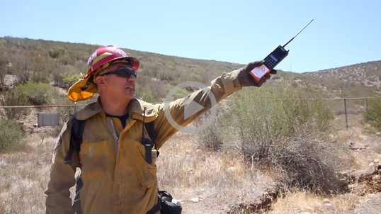 A wildland fire fighter points to the distance with their radio