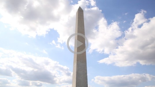 A tall obelisk monument towers into a blue sky with clouds
