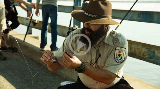 A US Fish and Wildlife employee shows a Latino Conservation Week participate how to bait their fishing line