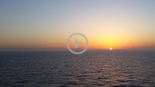 Wind turbines dot the skyline in the ocean as the sun sets