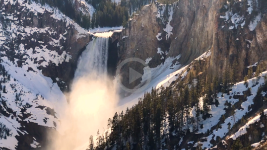 A waterfall cascades through snowy mountains.