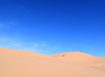 Sand dunes and a blue sky, with an OHV in the distance. 