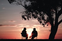 Two people sitting in chairs watching the sun set.