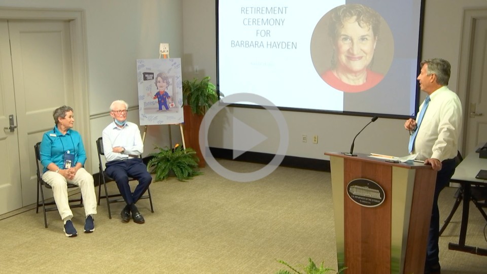 A retiring nurse sits in a chair at their retirement ceremony