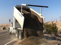 A dump truck drops gravel on the side of the road. 