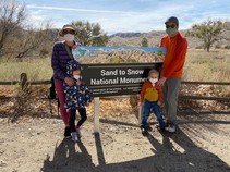 A family wearing masks standing by the Sand to Snow National Monument. 